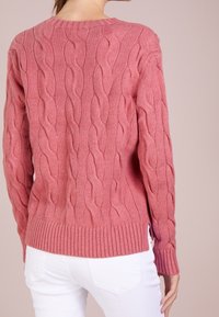 Pull en maille torsadée de couleur rose doux, avec un ourlet et des poignets côtelés. Le dos présente un motif complexe et des fentes latérales à l'ourlet.