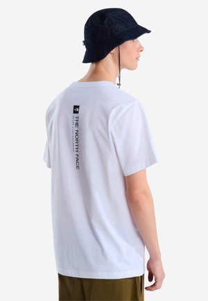 Young man wearing a white The North Face T-shirt and a black bucket hat, shown from the back and side against a plain background.