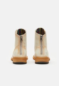 Botas de tobillo de marfil con un diseño perforado, cremalleras plateadas y una suela de madera. Forradas con una tela de rayas coloridas.