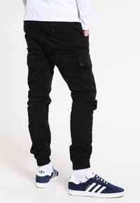 Svarta cargobyxor med flera fickor och knappar, smal passform, kombinerade med blåa och vita sneakers samt vita ankelsockor.