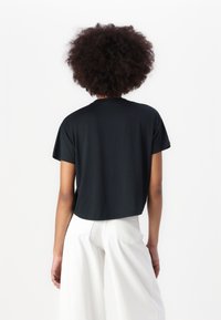 T-shirt nera corta con maniche corte, scollatura rotonda e texture morbida. Abbinata a pantaloni bianchi a gamba larga. Design minimalista.