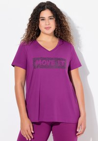 Kort lilla V-hals t-shirt i blødt stof med korte ærmer. Har et sort grafisk tekstdesign på forsiden.