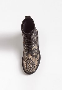 Bottine en dentelle noire avec une tige en dentelle à motif sur une base beige contrastante, des œillets noirs et une boucle en tissu au talon.