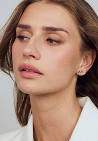 Silverörhängen i form av tre graderade sfärer, bar av en person med långt hår, ljus hy och naturlig makeup. Enkelt design.