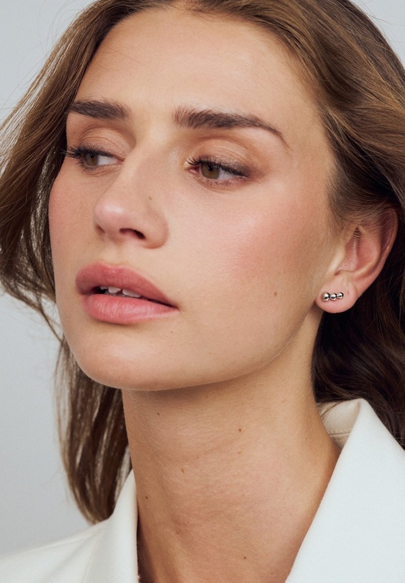 Silverörhängen i form av tre graderade sfärer, bar av en person med långt hår, ljus hy och naturlig makeup. Enkelt design.