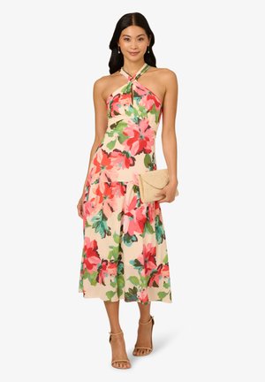 Blumenkleid in Midi-Länge mit einem Neckholder-Design, lebhaften pinken und grünen Mustern auf einem cremefarbenen Hintergrund, ergänzt durch eine beigefarbene Clutch.