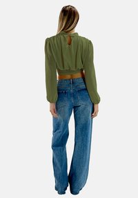 Blusa corta verde oliva con maniche a sbuffo e dettaglio a chiave sul retro, abbinata a jeans a vita alta di colore blu chiaro, con vestibilità ampia.