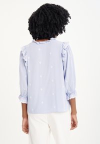 Blusa azzurro chiaro con maniche a sbuffo, bordi in pizzo e intricati motivi ricamati. Vestibilità rilassata con dettagli arricciati ai polsini.