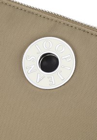 Portafoglio in tessuto beige con texture, dotato di una chiusura zip e di un elegante hardware circolare argentato con il nome del brand, e un accento centrale nero.