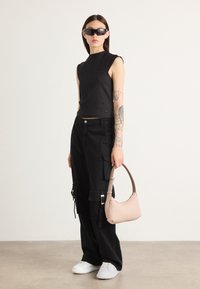 Black cropped tank top, black cargo pants with pockets, white sneakers, and a beige handbag with a curved handle. Smooth textures, minimalist design.