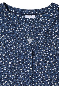 Blouse bleu marine avec un motif léopard dans des nuances de bleu variées, dotée d'un décolleté en V et de trois boutons bleus.