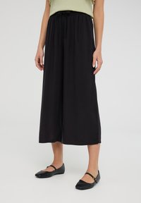 Culotte neri, larghi e comodi, con vita elastica e cordoncino. Indossati con scarpe basse nere, che mettono in evidenza un design semplice e versatile.