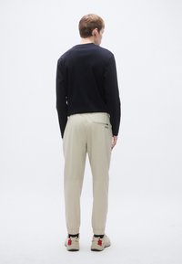 Fekete hosszú ujjú felső és bézs színű, gumis mandzsettás, szűk szárú nadrág. A nadrág hátulján márkajelzéssel ellátott zseb és húzózsinóros derékrész található.