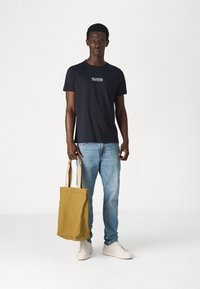 T-shirt navy con logo, jeans azzurri, sneakers crema e borsa tote gialla in tela. Design semplice e vestibilità casual.