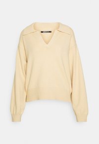 Krämfärgad V-halskofta med krage, långa puffärmar och ribbad nederkant. Tillverkad av mjukt, texturerat tyg.