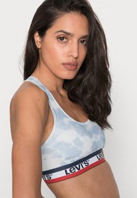 Ljusblått tie-dye-bh-top med svart och röd elastisk band med "Levi's"-logotyp. Slät textur och racerback-design.