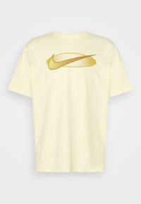 Camiseta de algodón amarilla con un gran logo de Nike en dorado que presenta patrones de puntos en la parte frontal. Mangas cortas y diseño de corte relajado.