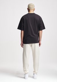 Schwarzes Baumwoll-T-Shirt mit lockerer Passform, kurzen Ärmeln und Rundhalsausschnitt, kombiniert mit cremefarbenen Jogginghosen und weißen Sneakern.