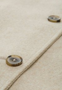 Barna gyapjú anyag, puha textúrával, két kerek, áttetsző gombbal sötétebb árnyalatban, középen gomblyuk öltéssel.