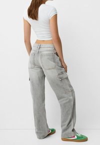 Pantalones cargo gris claro con bolsillos laterales y un ajuste relajado. Combinados con una blusa blanca ajustada y zapatillas de colores.