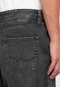 Temno sivi jeans iz denima z nalepko z utisnjenim logotipom, kontrastnim šivom in eno zadnjo žepno z ukrivljenim šivom.