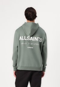 Green hoodie with a relaxed fit, featuring a large white "ALLSAINTS" logo on the back, and text in Japanese and "LONDON" underneath.