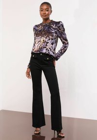 Ilgi piedurkņu blūze purpura krāsā ar ziedu rakstiem, saskaņota ar augsto vidukli melnām plānu flared biksēm, kurām ir zelta tonos pogas. Gludas tekstūras.