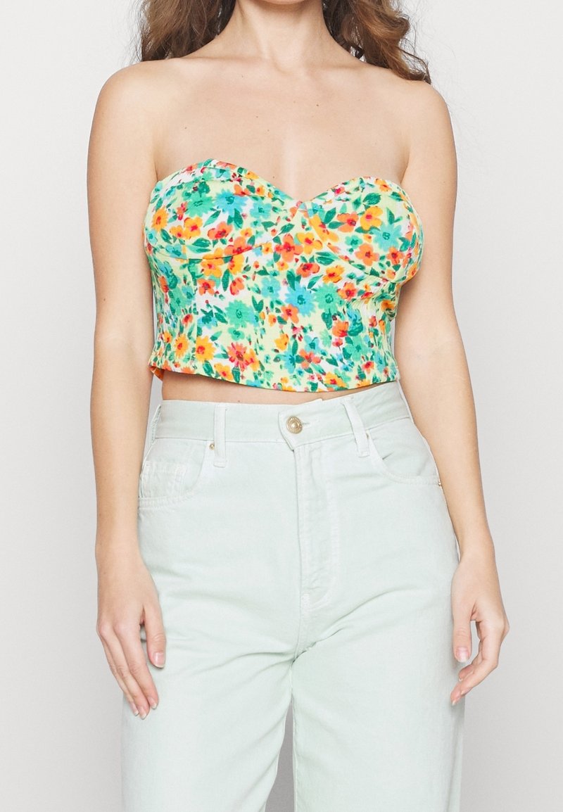 Květinový crop top s výstřihem do srdce v zelených, žlutých a červených odstínech; nošený s světlými mentolovými džíny s vysokým pasem.