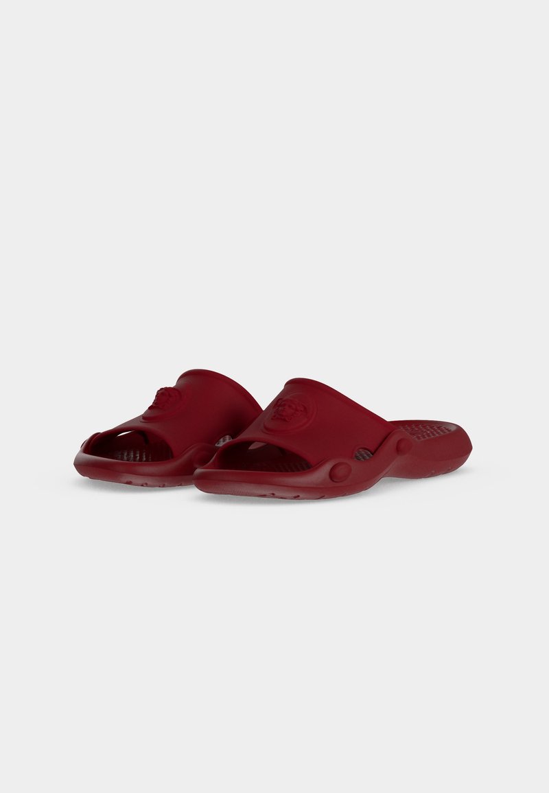 Pair of red open-toe slide sandals with a textured footbed and a raised emblem on the top strap, shown on a white background.