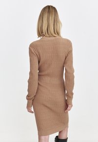 Dres swetrowy dzianiny w jasnobrązowym kolorze z prążkowaną fakturą, dopasowaną talią, długimi rękawami i okrągłym dekoltem. Projekt o długości midi.