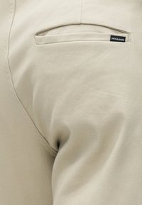 Pantalons en coton beige avec une texture lisse, comportant une poche arrière et un petit onglet noir avec le logo "JACK & JONES."
