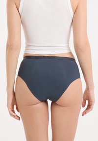 Culotte taille haute bleu marine avec une texture lisse et une ceinture subtilement pailletée. Design simple sans motifs ni accessoires visibles.