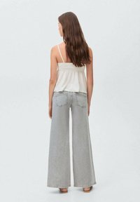 Ljust grå vida jeans och en vit ärmlös topp med en samlad nederkant. Tyget ser mjukt ut; passformen är lös och avslappnad.