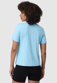 Světle modré tričko s krátkým rukávem vyrobené z měkkého materiálu, s kulatým výstřihem a uvolněným střihem, nošené s černými upnutými šortkami.