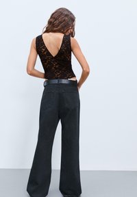 Body in pizzo nero con schiena a V profonda, abbinato a jeans neri a vita alta e gamba larga con due tasche posteriori e una cintura nera.