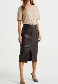 Beige tričko s krátkým rukávem spárované s těsnou, tmavě hnědou koženou tužkovou sukni s předním rozparkem, doplněné hnědými lodičkami na vysokém podpatku.