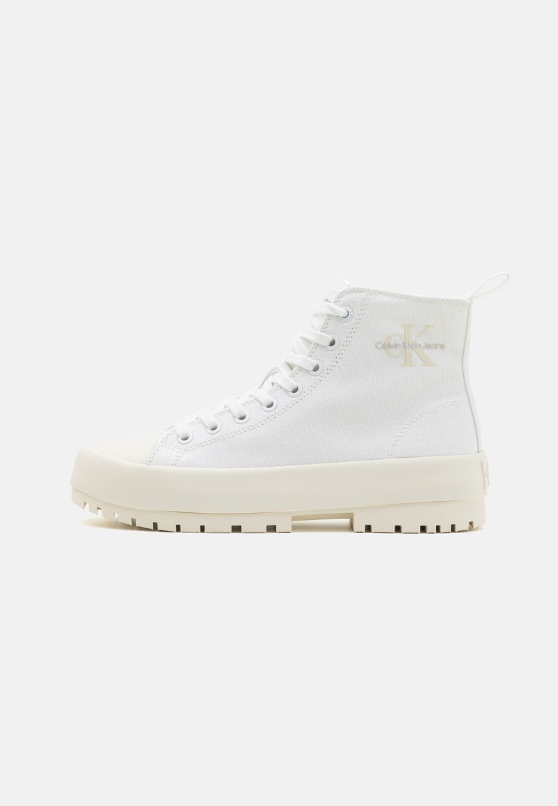Zapatillas altas de lona blanca con un acabado texturizado, cordones planos y una suela de goma gruesa. Logo icónico en relieve en dorado en el lateral.
