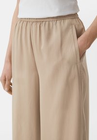 Beige Hose mit weitem Bein, elastischem Bund und seitlichen Taschen, aus leichtem, glattem Stoff und mit geradem Schnitt.