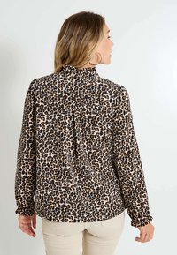 Blouse imprimé léopard avec un col haut, des manches longues et des poignets froncés. Conçue en tissu léger, elle présente une coupe légèrement décontractée et un détail au dos.