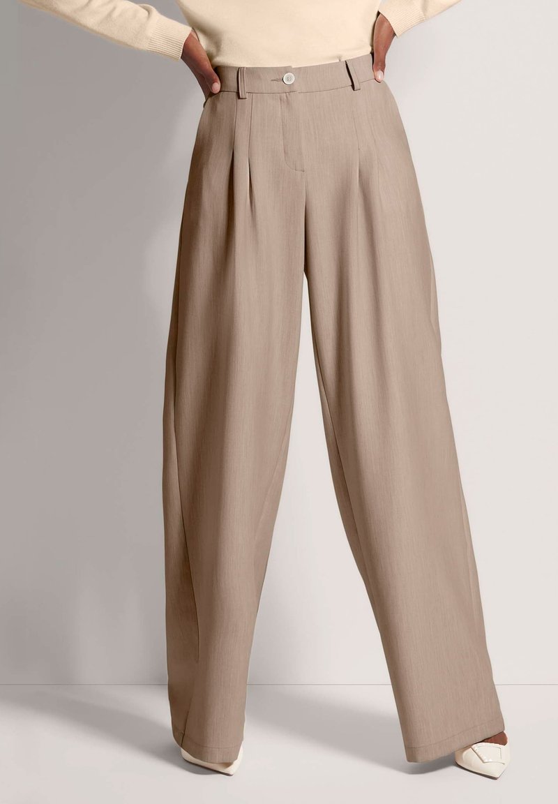 Beige wijde broek met plooien, gemaakt van een textuurstof. Voorzien van een knoopsluiting en een gestructureerde tailleband, gestyled met puntige schoenen.