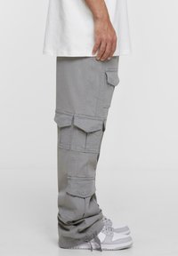 Pantaloni cargo gri cu multiple buzunare frontale și laterale, croi lejer și un design ușor conic al piciorului, asortați cu adidași albi.