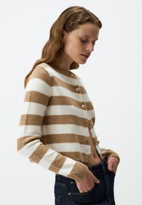 Gehaakte cardigan in beige en witte strepen, met een ronde hals, vijf knopen en geribbelde manchetten. Zachte textuur met een cropped ontwerp.