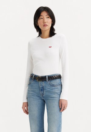 Biała bluzka z długim rękawem z małym czerwonym logo Levi's, zestawiona z jasnoniebieskimi spodniami o wysokim stanem i czarnym plecionym paskiem. Prosty fason, miękka tekstura.