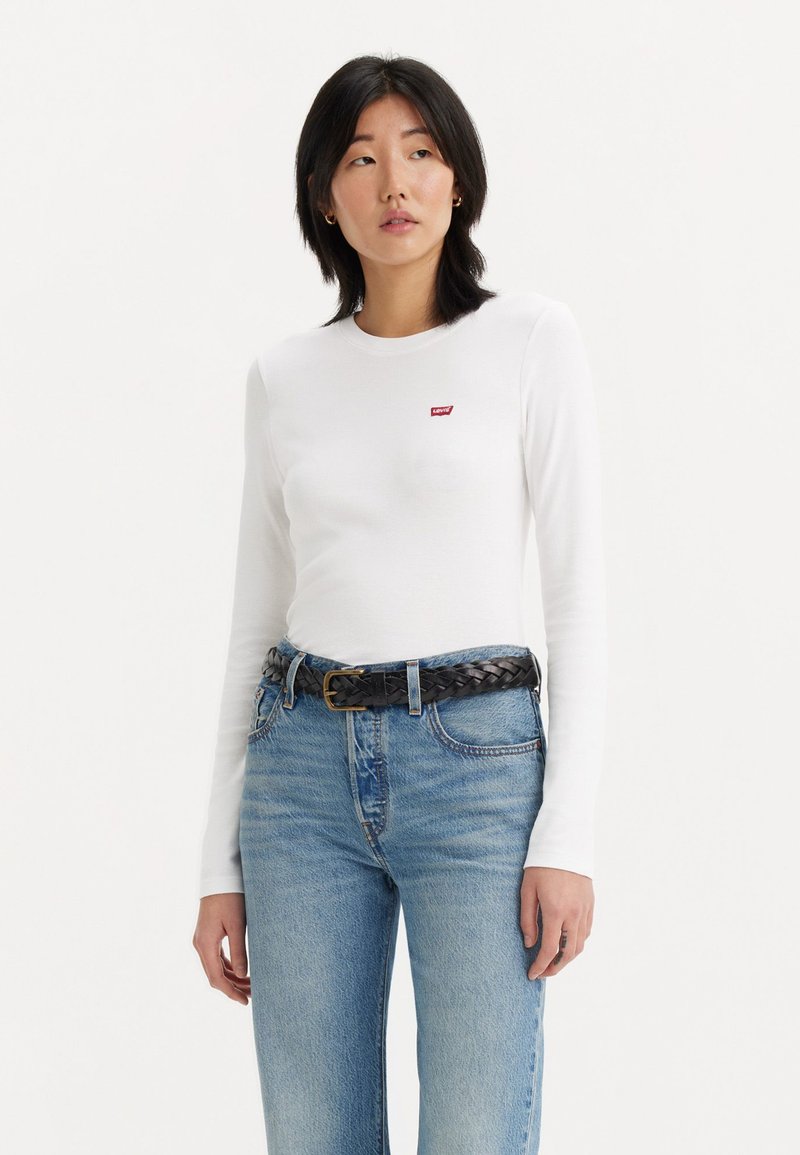 Weißes langärmliges T-Shirt mit kleinem roten Levi's-Logo, kombiniert mit hellblauen hoch taillierten Jeans und einem schwarzen geflochtenen Gürtel. Schlichtes Design, weiche Textur.