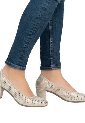 Perforierte, hellbeige High Heels mit runder Spitze, etwa 5 cm Blockabsatz, getragen mit dunkelblauen Skinny Jeans.