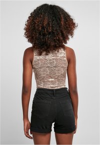 Top sin mangas de encaje en beige con un patrón floral, combinado con unos pantalones cortos de mezclilla negros de cintura alta. La textura parece suave.