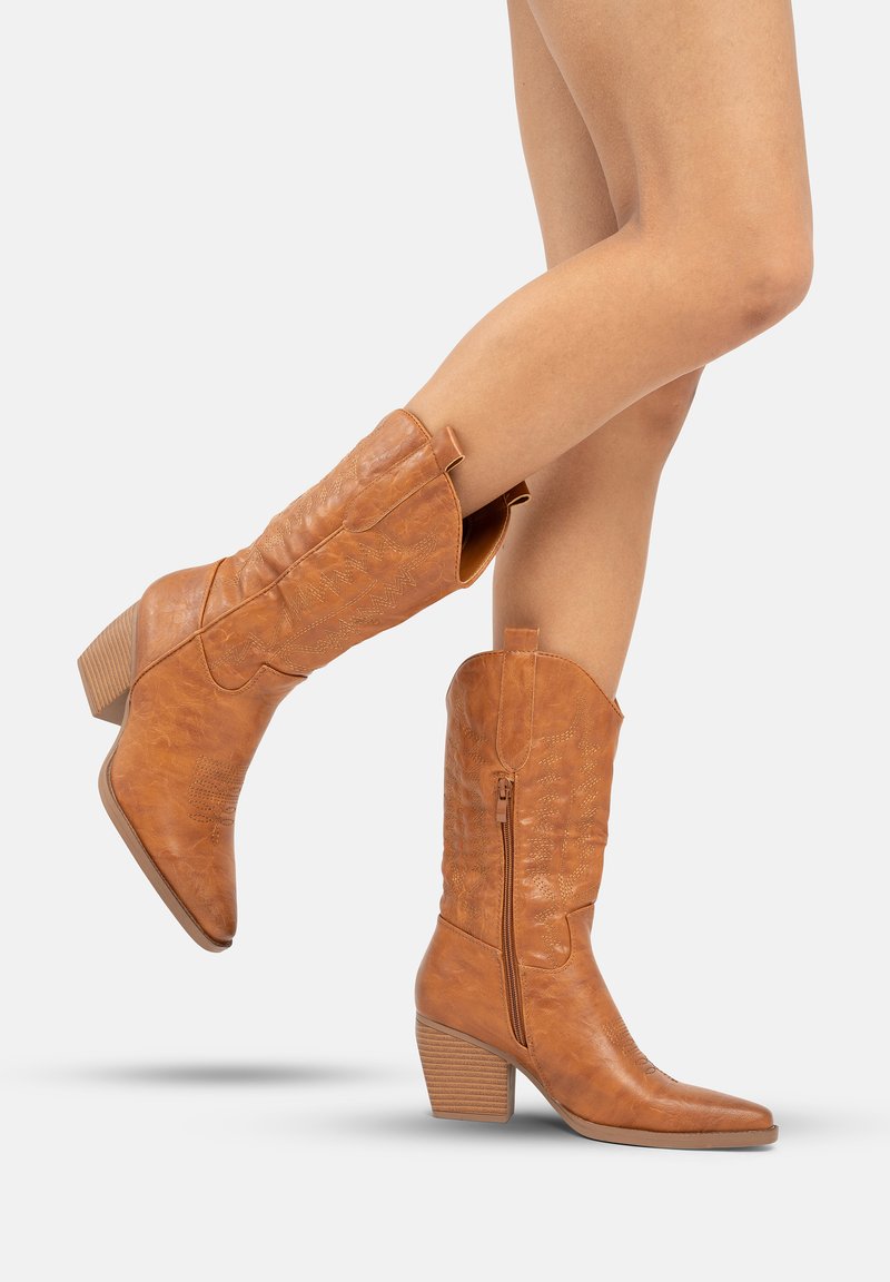 Botas de vaquero de cuero marrón con punta afilada, tacón estriado, costuras decorativas y detalle de cremallera lateral. Textura suave, altura hasta la mitad de la pantorrilla.