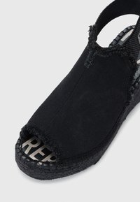 �Černé plátěné espadrilky s otevřenou špičkou, okraje na svršku jsou třepené a podrážka je z pleteného juty. Vnitřní stélka nese výrazné logo.