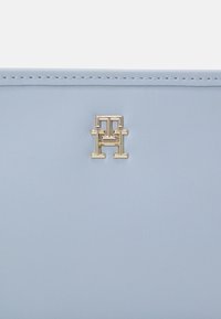 Portafoglio in pelle azzurro chiaro con logo dorato impresso a caldo con lettere intrecciate e una finitura opaca liscia. La cucitura è visibile lungo i bordi.