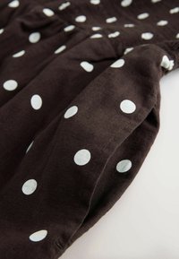 Material maron cu buline albe mari, cu o textură moale și un design strâns, punând în evidență un model jucăuș, cu un contrast puternic.